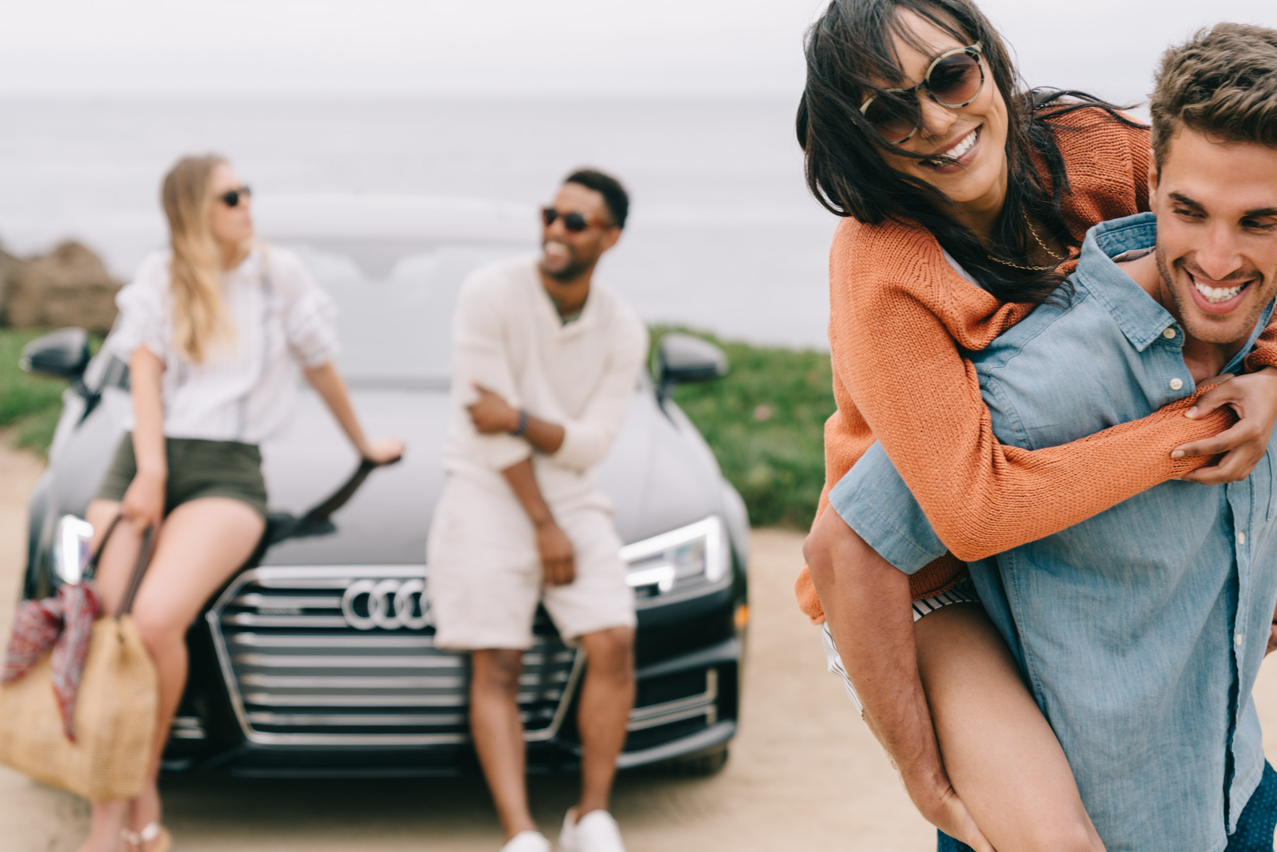 Four friends goofing around by their black Audi A3 at the beach