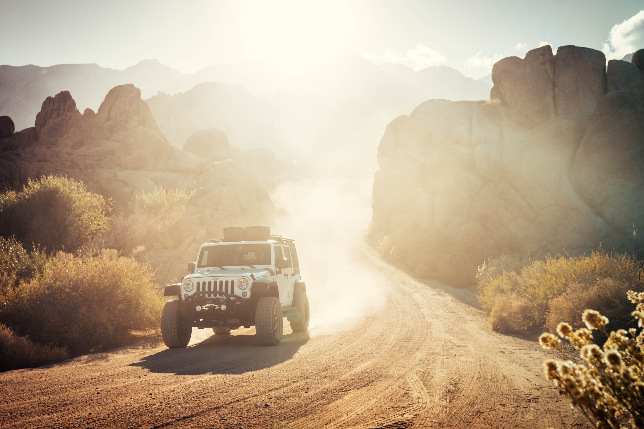 White Jeep driving down dusty dirt road in the Alabama Hills