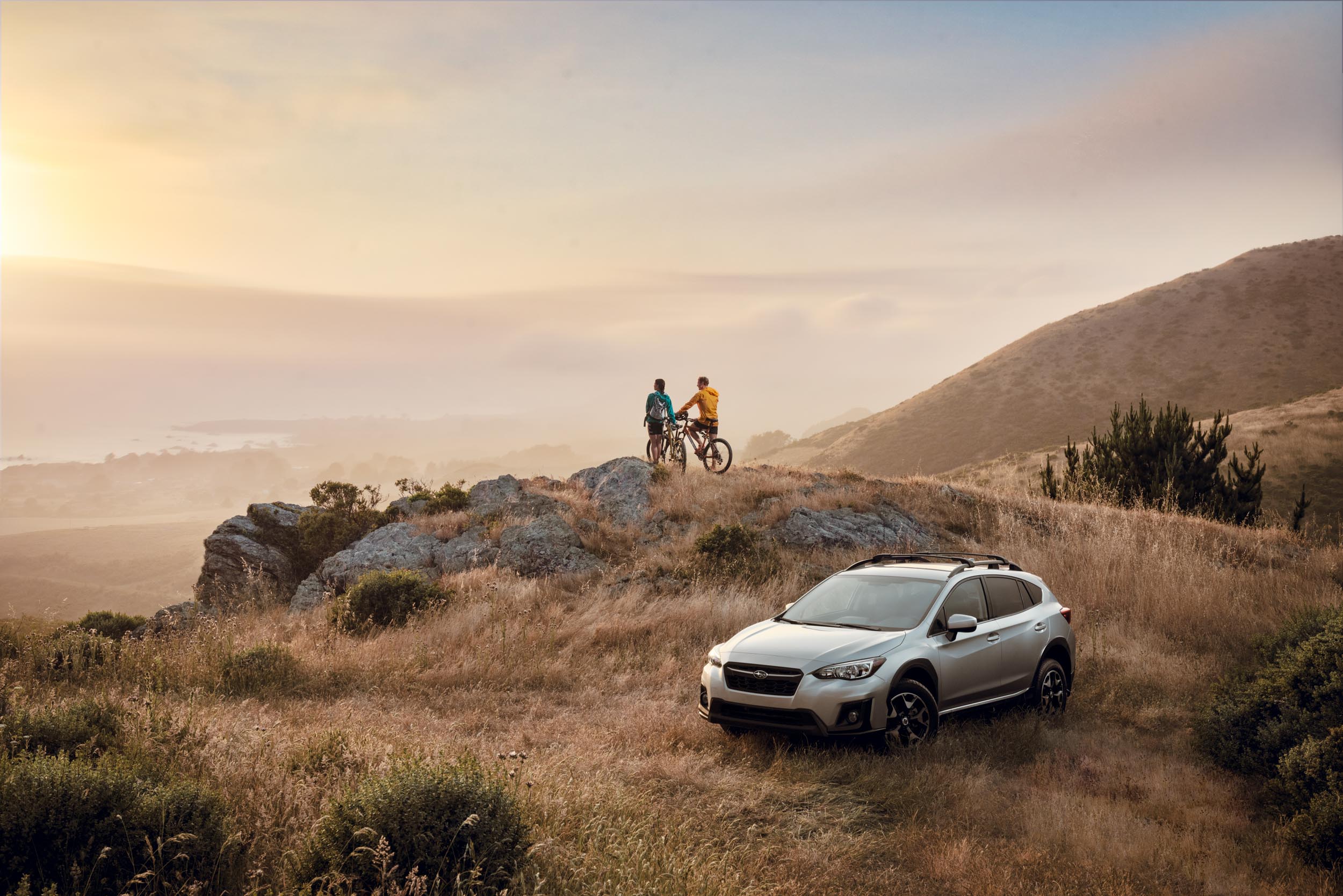 Two mountain bikers watch the sunset near their Subaru Crosstrek