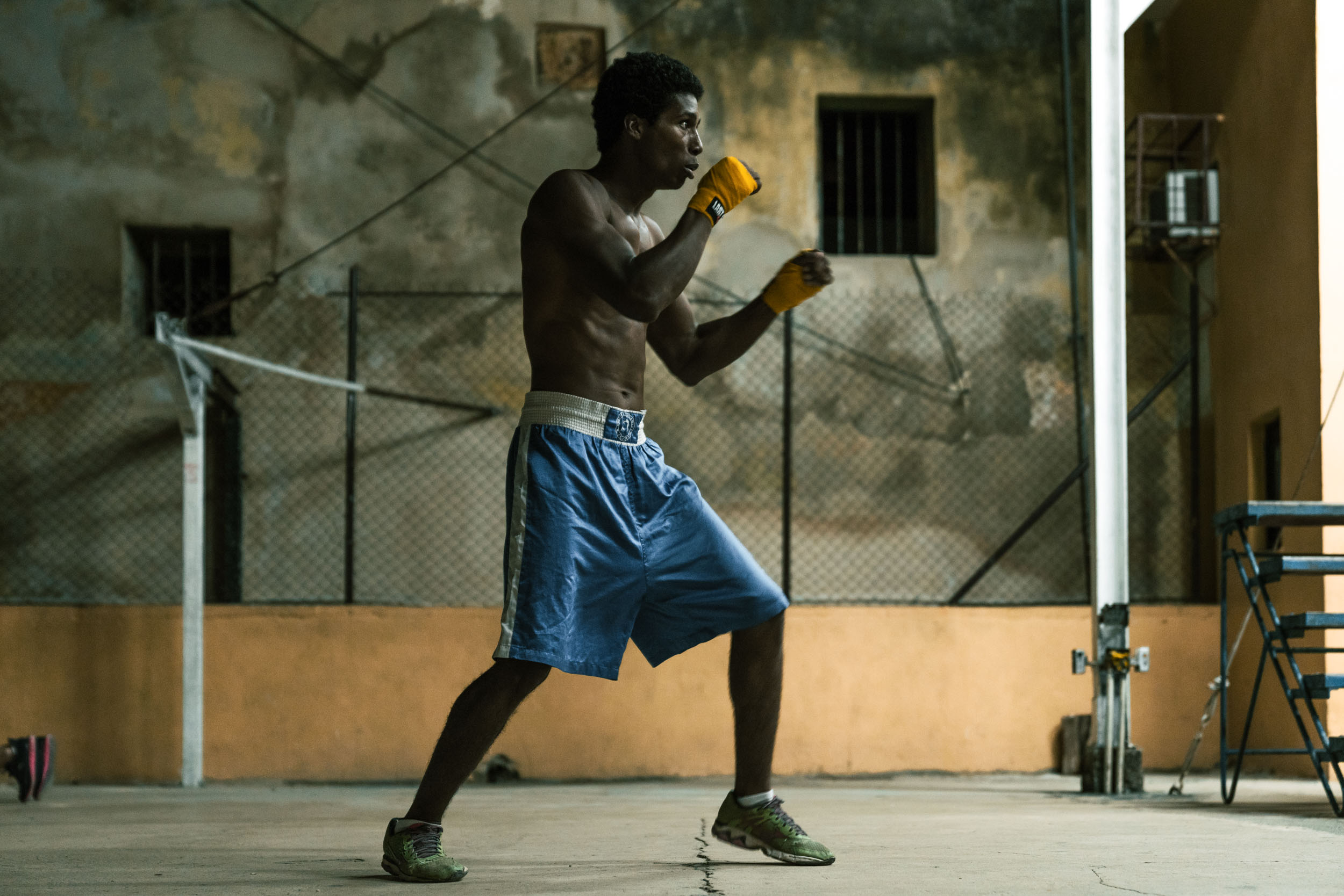 Male boxer in blue shorts shadow boxes in a dark boxing gym in Havana Cuba