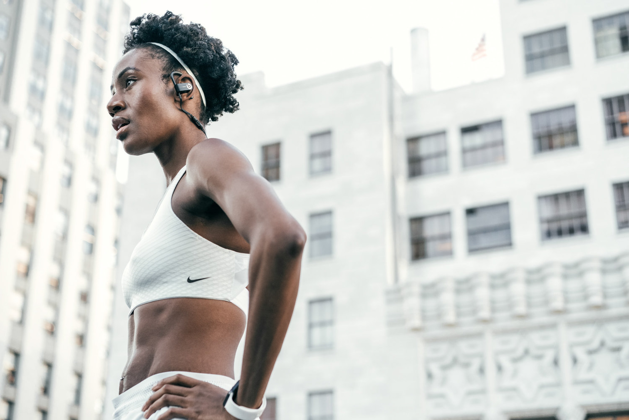 Female athlete in white Nike sports bra and shorts stands with hands on hips and looks into the distance