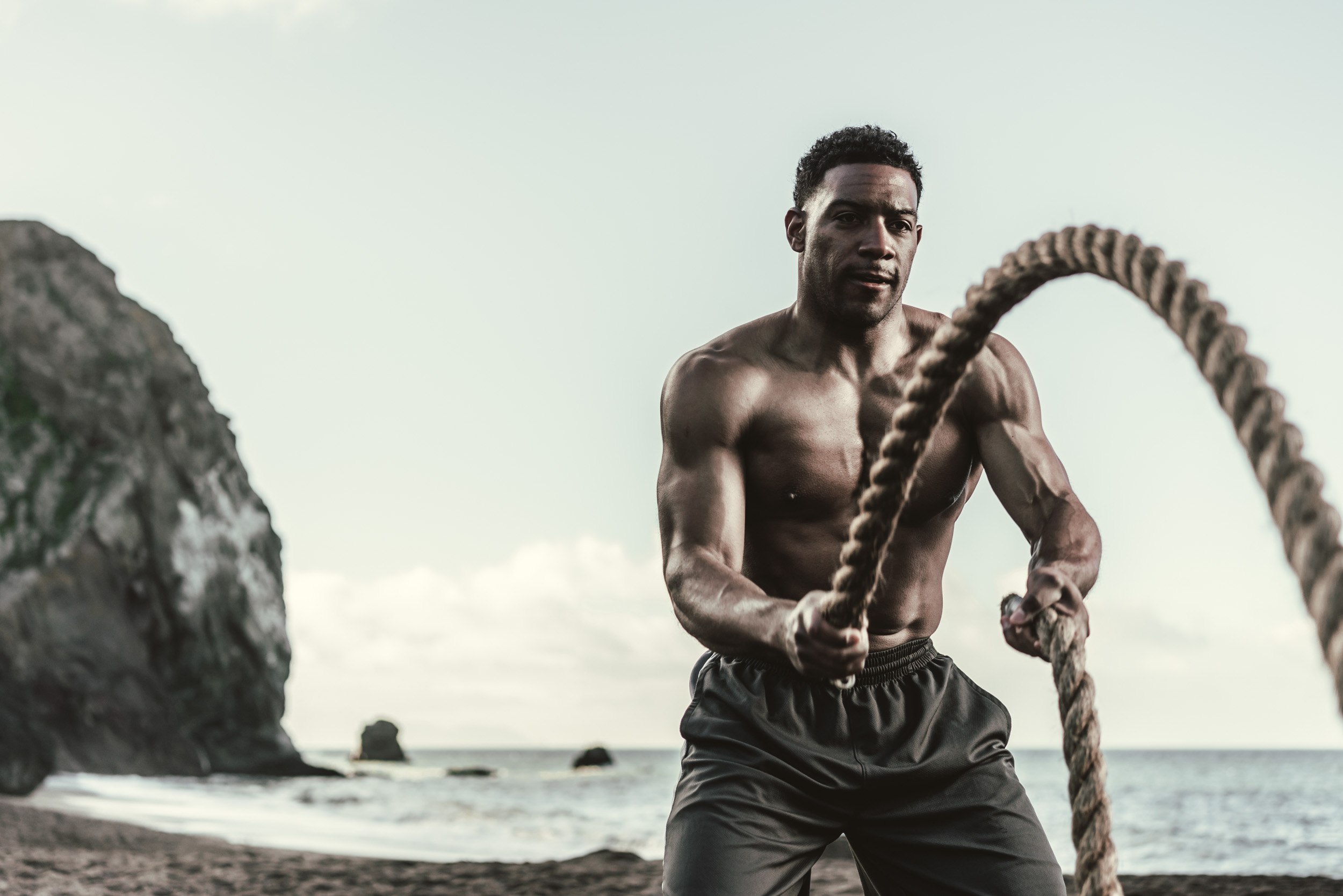 Male athlete  with no shirt uses battle ropes while working out on the rocky Tennessee Beach
