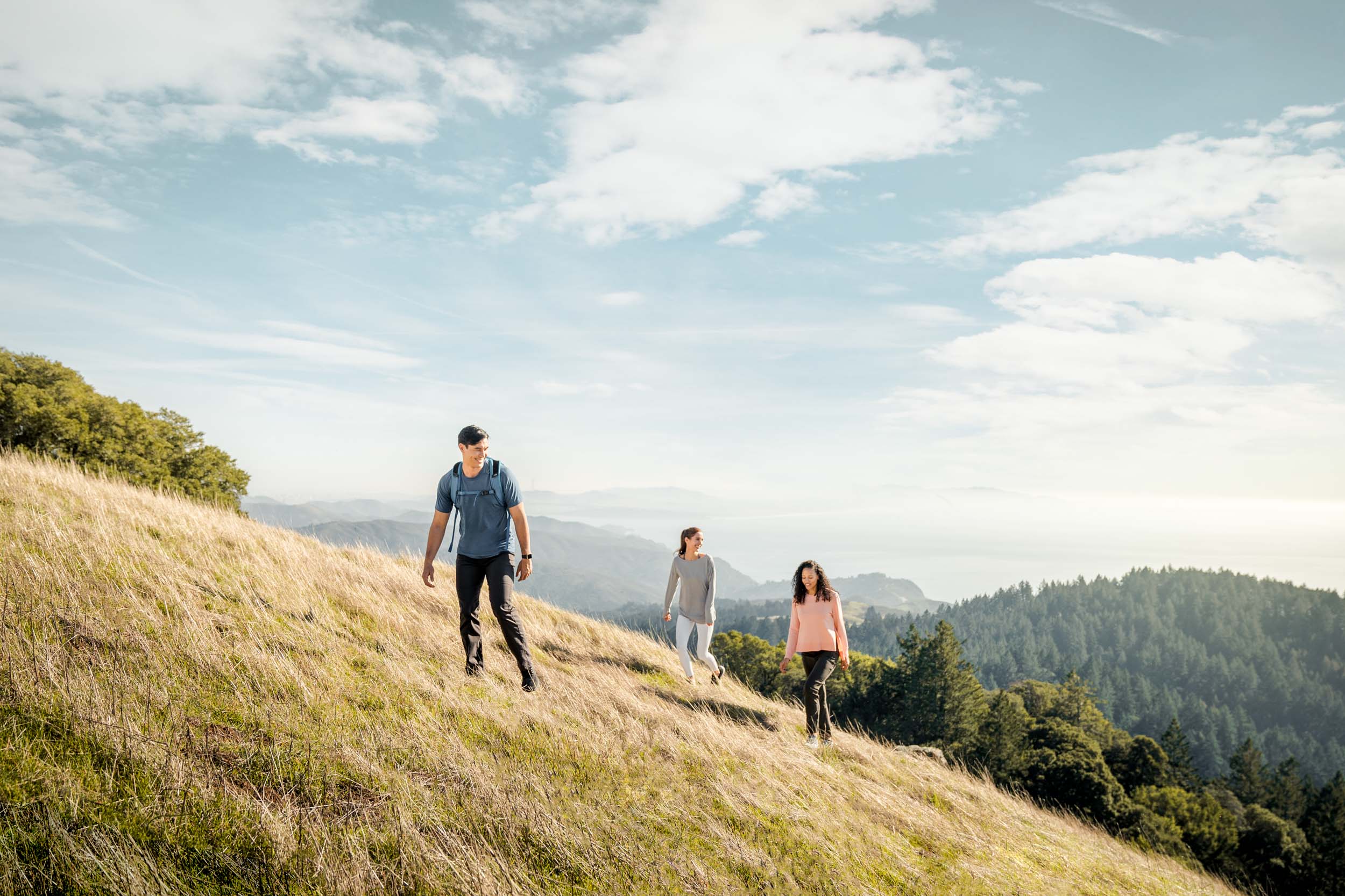Three friends walk up a hill on tall golden grass near Mt Tam with the ocean in the background